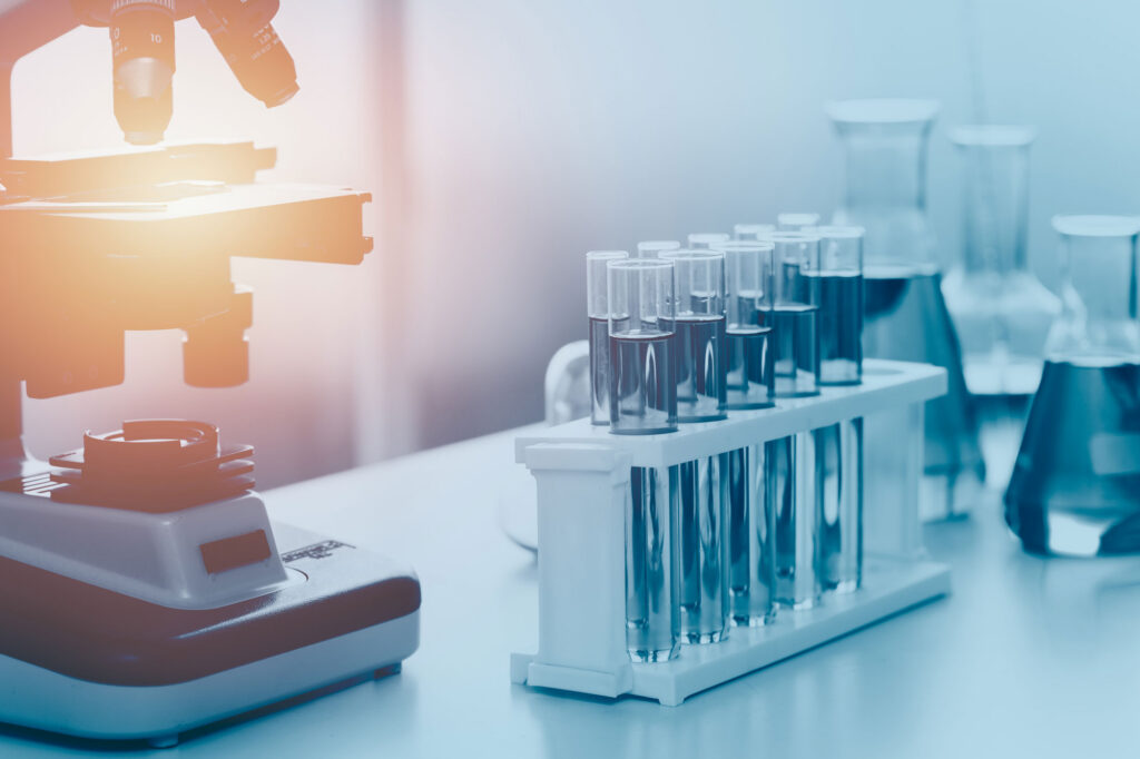 Laboratory scene with a microscope on the left and a rack of test tubes filled with liquid on the bench in the foreground