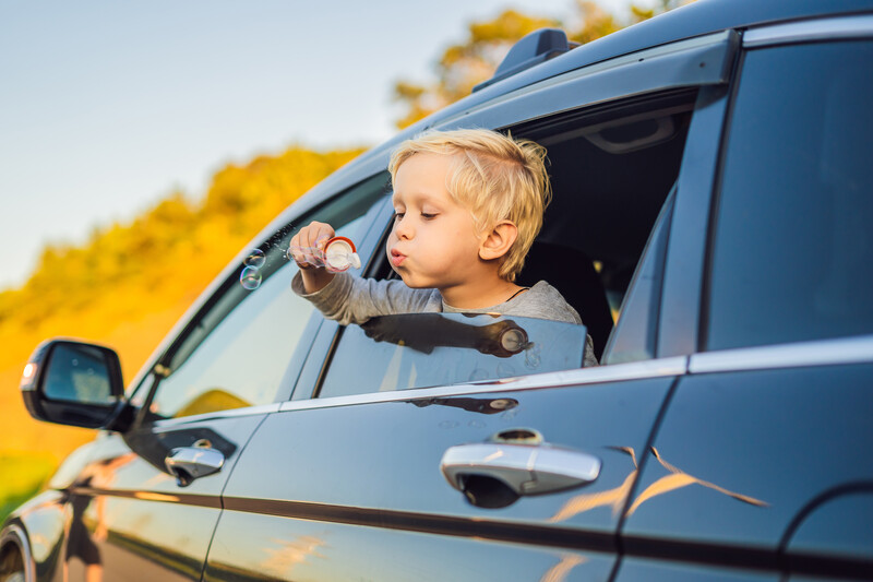 Boy in a car window blowing soap bubbles on a sunny day.
